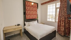 Quarto com cama, escrivaninha, espelho e janela com cortinas.