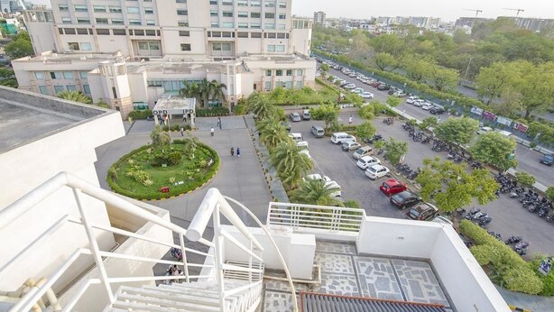 Um edifício com vários andares, um estacionamento e uma área ajardinada na frente.
