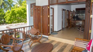 Un balcon en bois offrant une vue sur des palmiers, une table en bois et deux chaises en bois.