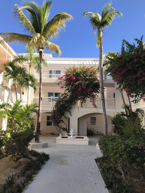 Escape to a tranquil oasis surrounded by lush palm trees and vibrant flowers, with a soothing fountain at its heart.