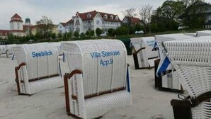 Beach chairs labeled 'Seeblick' and 'Villa Seeblick App.9' on a sandy area with buildings in the background.