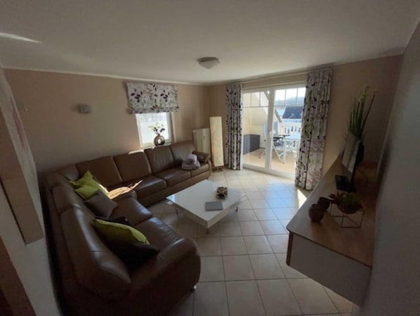A living room with a brown leather sofa, a white coffee table, and a view through a glass door to an outdoor area.