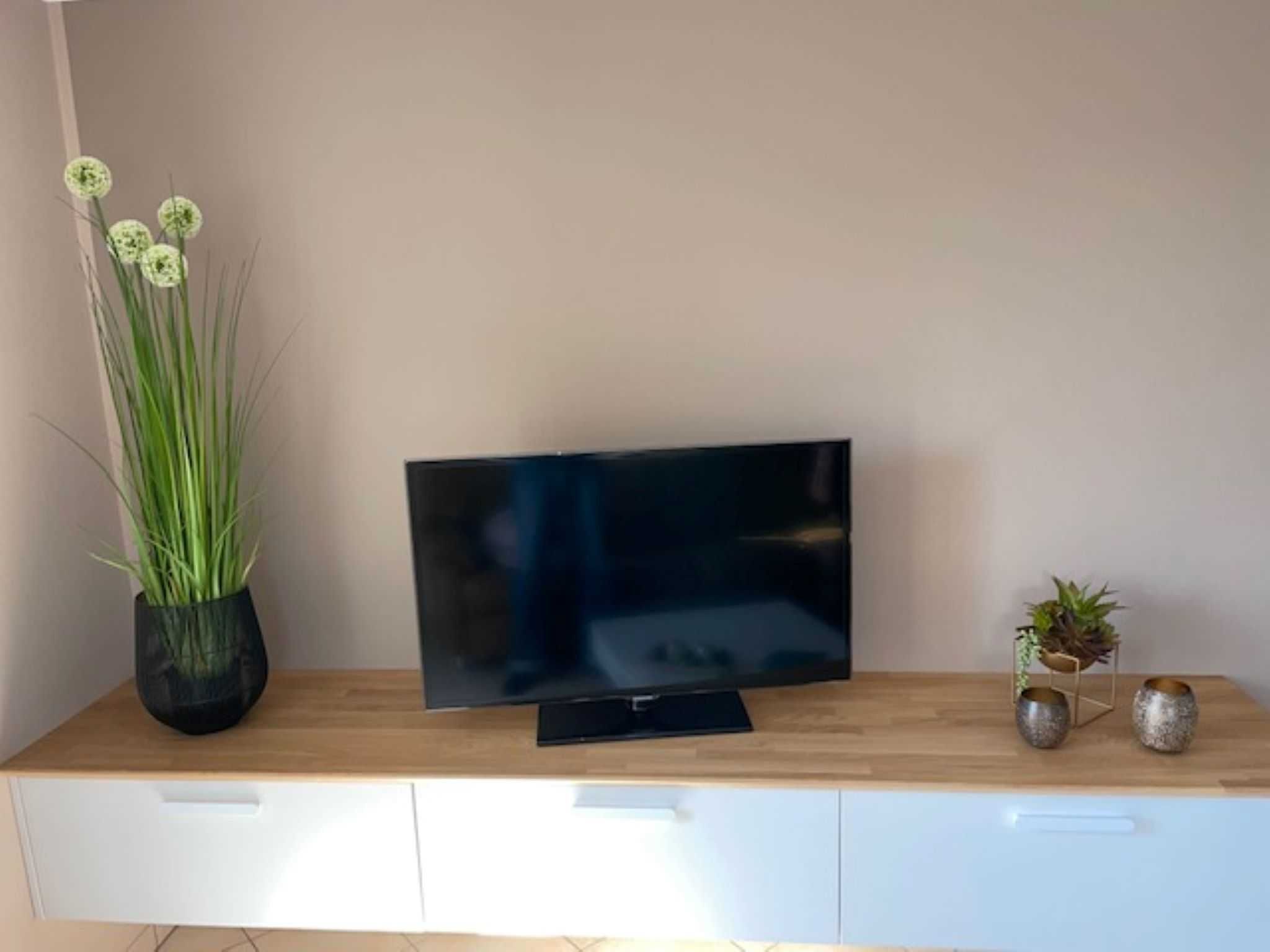 Un téléviseur à écran plat posé sur un meuble télé en bois, avec un tiroir blanc en dessous.