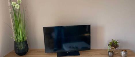 Un téléviseur à écran plat posé sur un meuble télé en bois, avec un tiroir blanc en dessous.