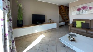 A living room with a TV, a sofa, a coffee table, and a staircase.