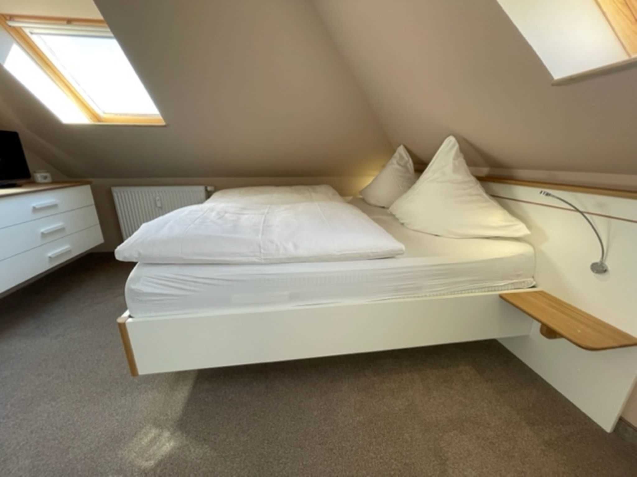 A bedroom with a bed, a desk, a chair, and a skylight.