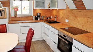 Cocina pequeña con armarios blancos, encimera de madera, microondas integrado, estufa y una sola silla roja.
