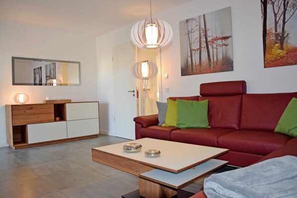 Un salon moderne avec un canapé rouge, une table basse en bois, un meuble blanc et un miroir au mur.