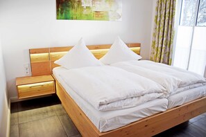 Un lit bien fait, avec du linge de lit blanc, une tête de lit en bois et une table de chevet dotée d’un tiroir.