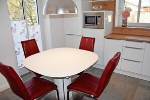 Une cuisine avec une table blanche et des chaises rouges, un four à micro-ondes et une fenêtre donnant sur des arbres.