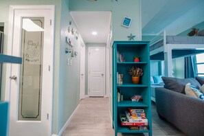 Une pièce avec une bibliothèque de couleur turquoise, un canapé gris et un lit superposé décoré d’une tortue.