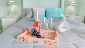 Cama bem arrumada com bandeja de madeira contendo garrafa, copos, uvas e toalha em forma de cisne.