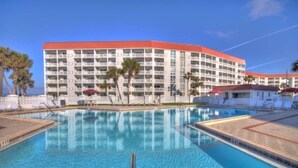 Um hotel com uma piscina grande, várias varandas e palmeiras.