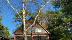 A rustic cabin with a wooden exterior, a porch with red Adirondack chairs, and a flagpole.