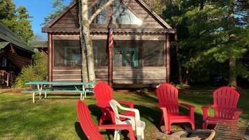 A rustic cabin with a wooden exterior, a porch with red Adirondack chairs, and a flagpole.