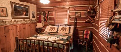Een knus houten blokhutkamer met een houten bed, een plafondventilator en een rustieke inrichting, waaronder ingelijste foto's en een geborduurde sprei.