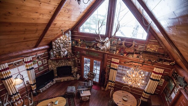 A cozy cabin with a stone fireplace, wooden furniture, and a large window offering a view of the outdoors.