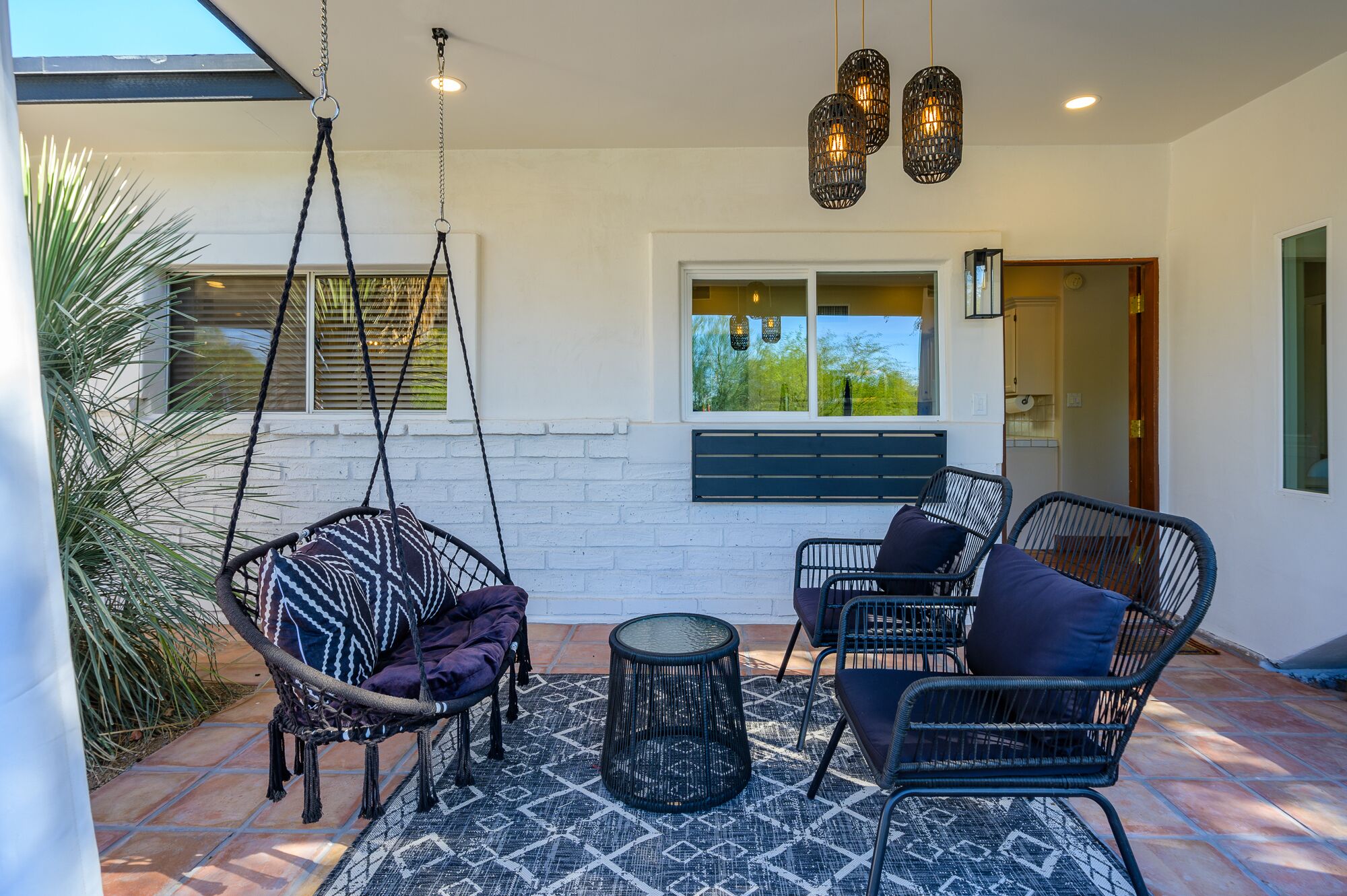A patio with wicker furniture, a hanging chair, and a patterned rug.