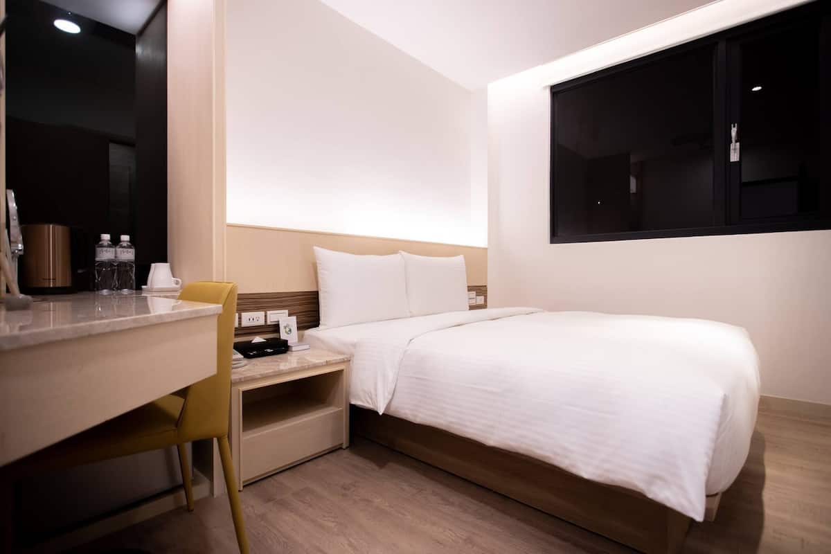 A hotel room with a bed, a desk, a chair, and a window.