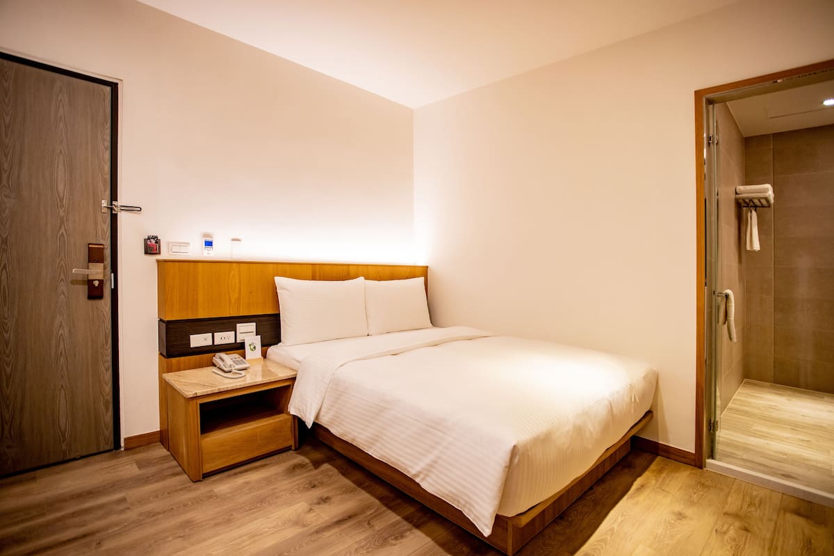 A hotel room with a wooden bed, a bedside table with a phone, and a glass-enclosed shower.