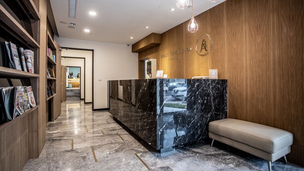 A reception area with a marble counter, wooden shelving with magazines, a bench, and a wooden wall with a logo. - Beauty Avenue Inn (Kaohsiung)