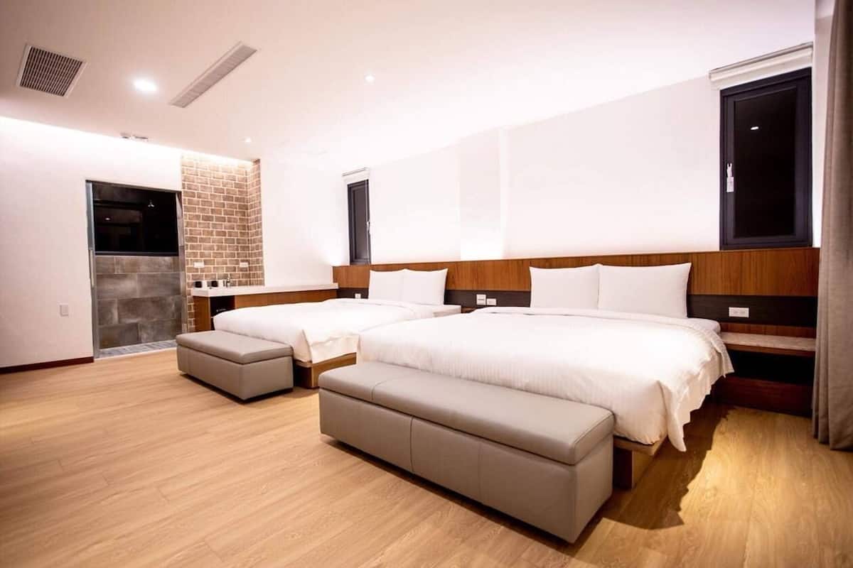 A modern hotel room with two beds, a small seating area, and a stone wall.