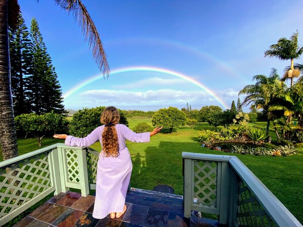 A person standing on a porch with a view of a garden and a rainbow.