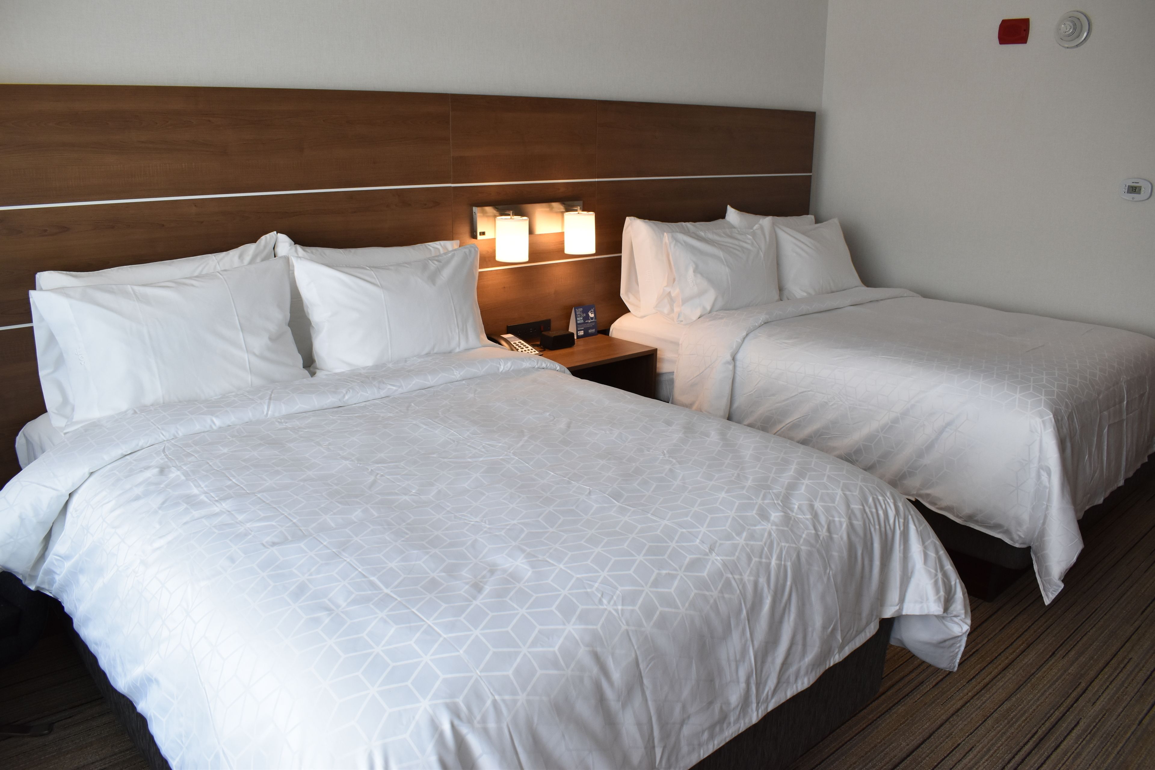 A hotel room with two beds, a wooden headboard, bedside lamps, and a nightstand.