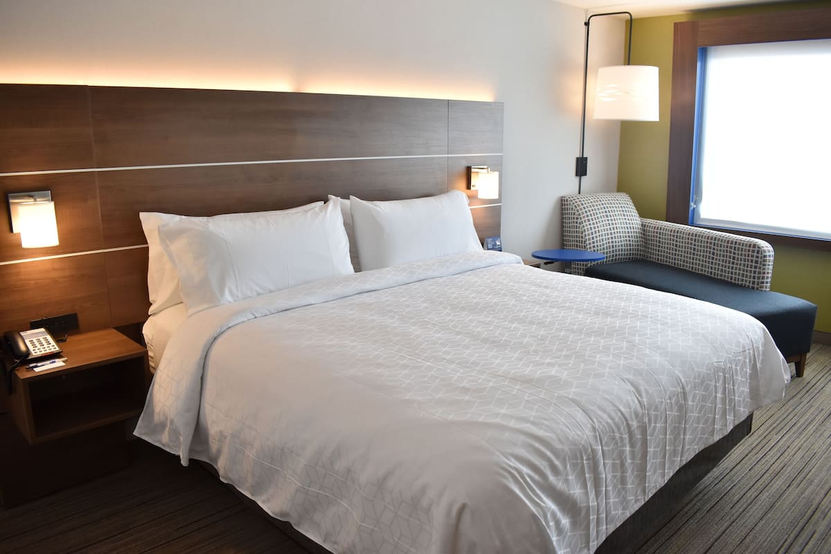 A hotel room with a large bed, bedside lamps, a small table, and a window with a view.