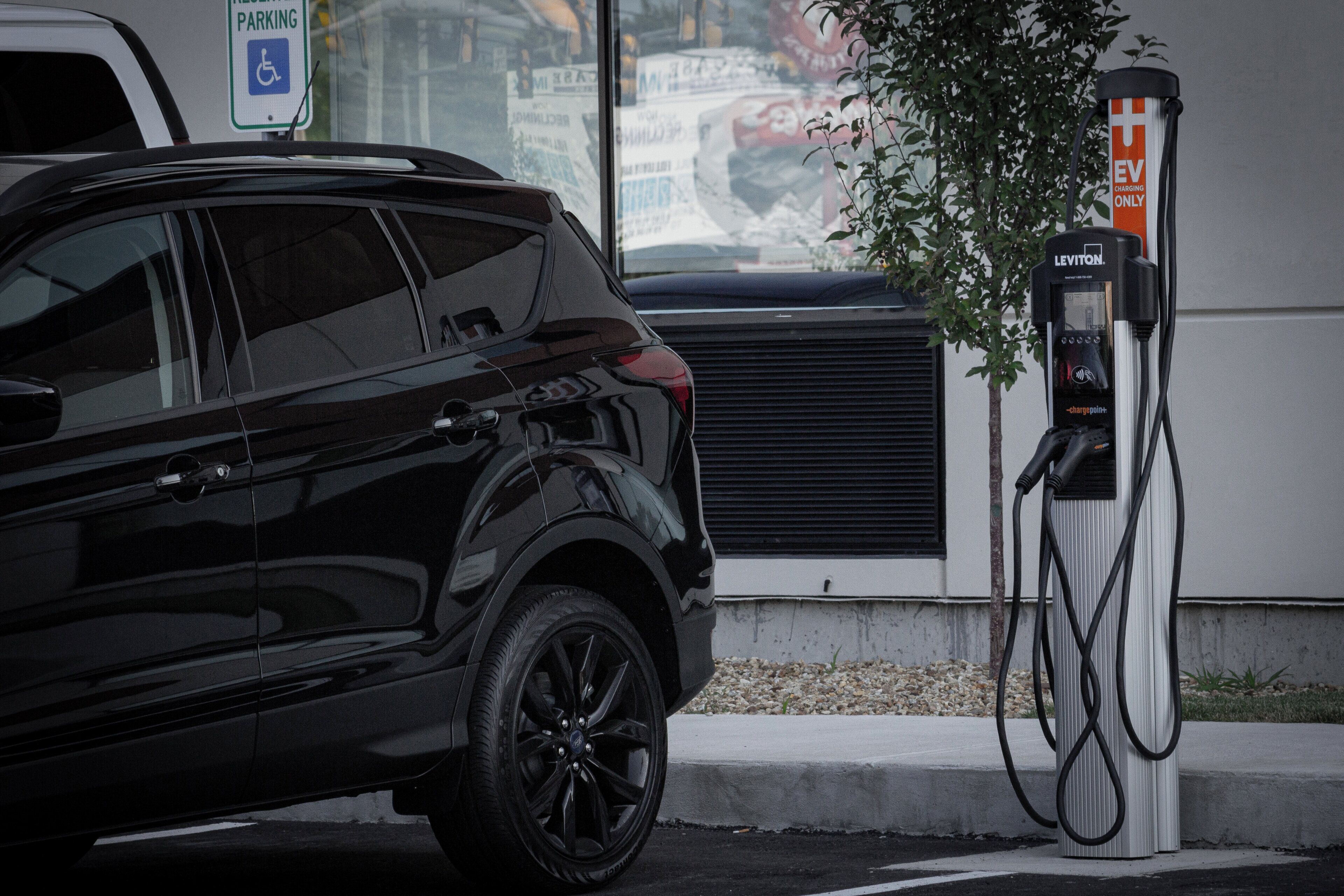 Un SUV negro estacionado junto a una estación de carga para vehículos eléctricos, con un letrero que indica que es una plaza reservada para personas con discapacidad.