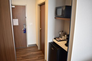 A narrow hallway with a wooden door, a microwave on a shelf, and a refrigerator. - Holiday Inn Express & Suites Boston South - Randolph by IHG (Randolph)
