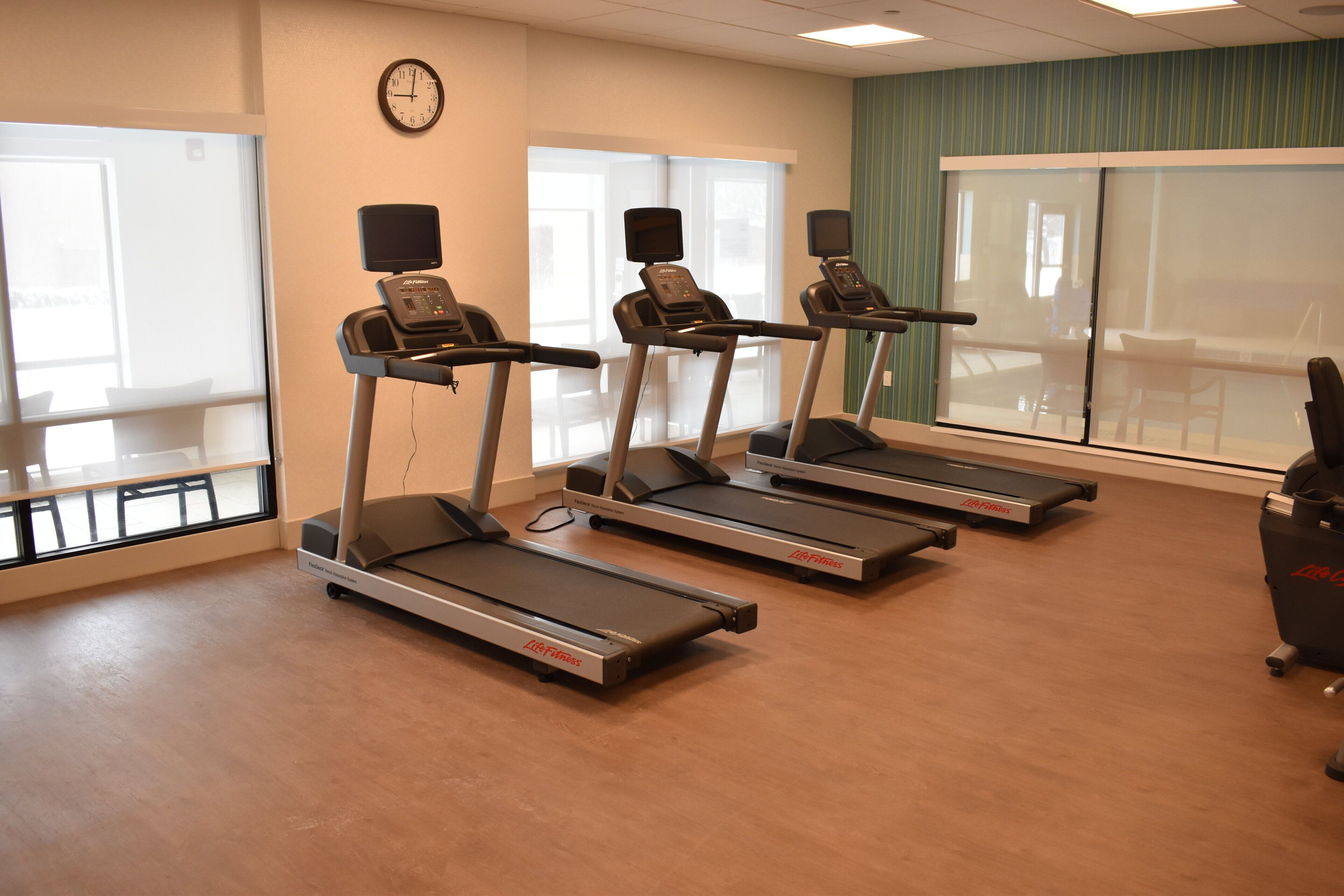 A fitness room with treadmills, a clock, and large windows.