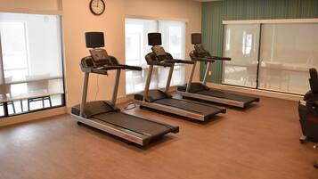 A fitness room with treadmills, a clock, and large windows.