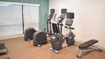 A gym with cardio machines, a bench, and a large window with curtains.