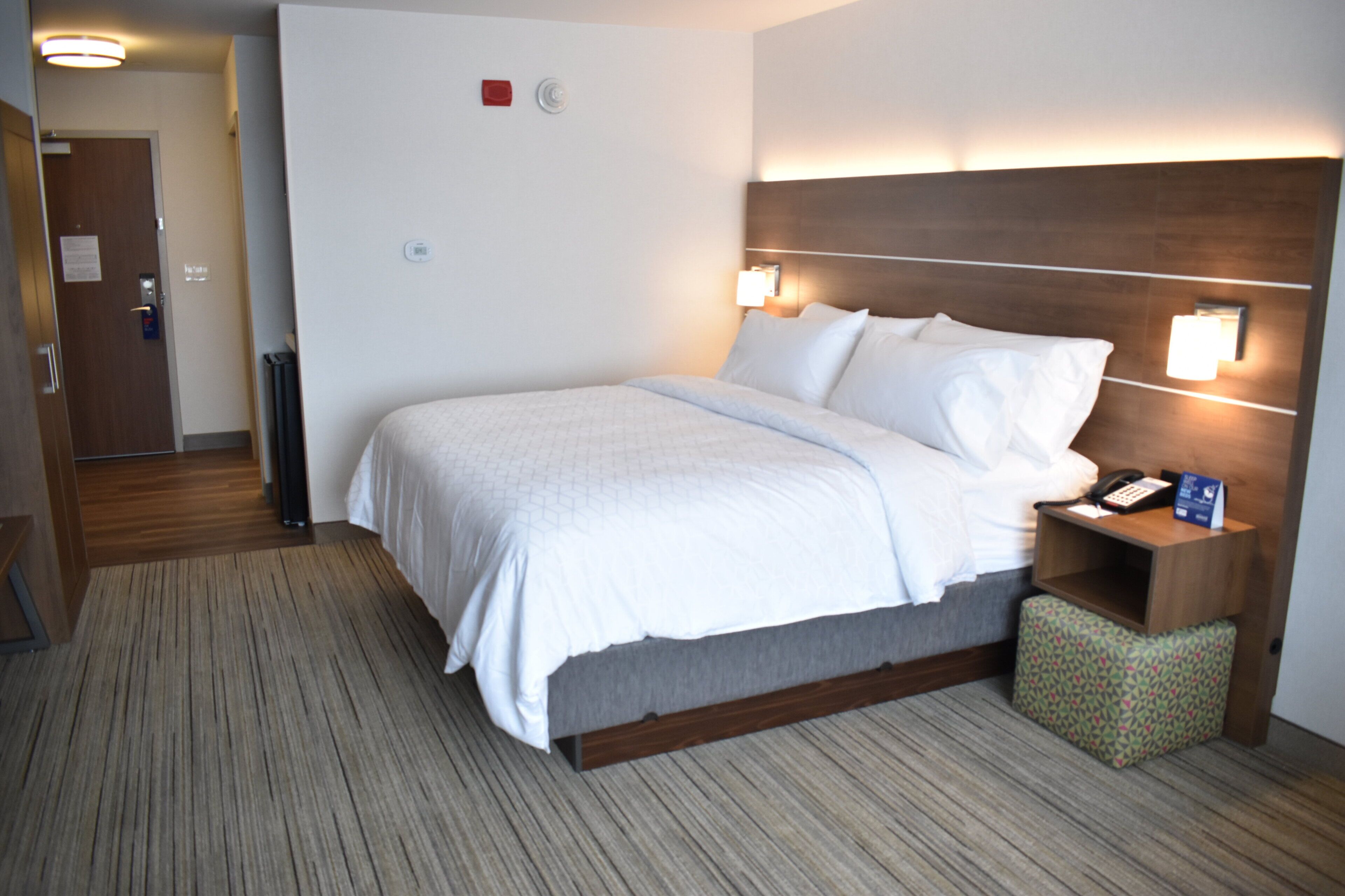A hotel room with a bed, bedside table, and a wall-mounted lamp.