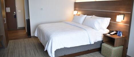 A hotel room with a bed, bedside table, and a wall-mounted lamp.