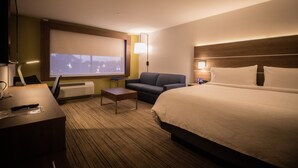 Une chambre d’hôtel avec un lit, un canapé, un bureau avec une lampe, une télévision et une fenêtre donnant sur la ville.