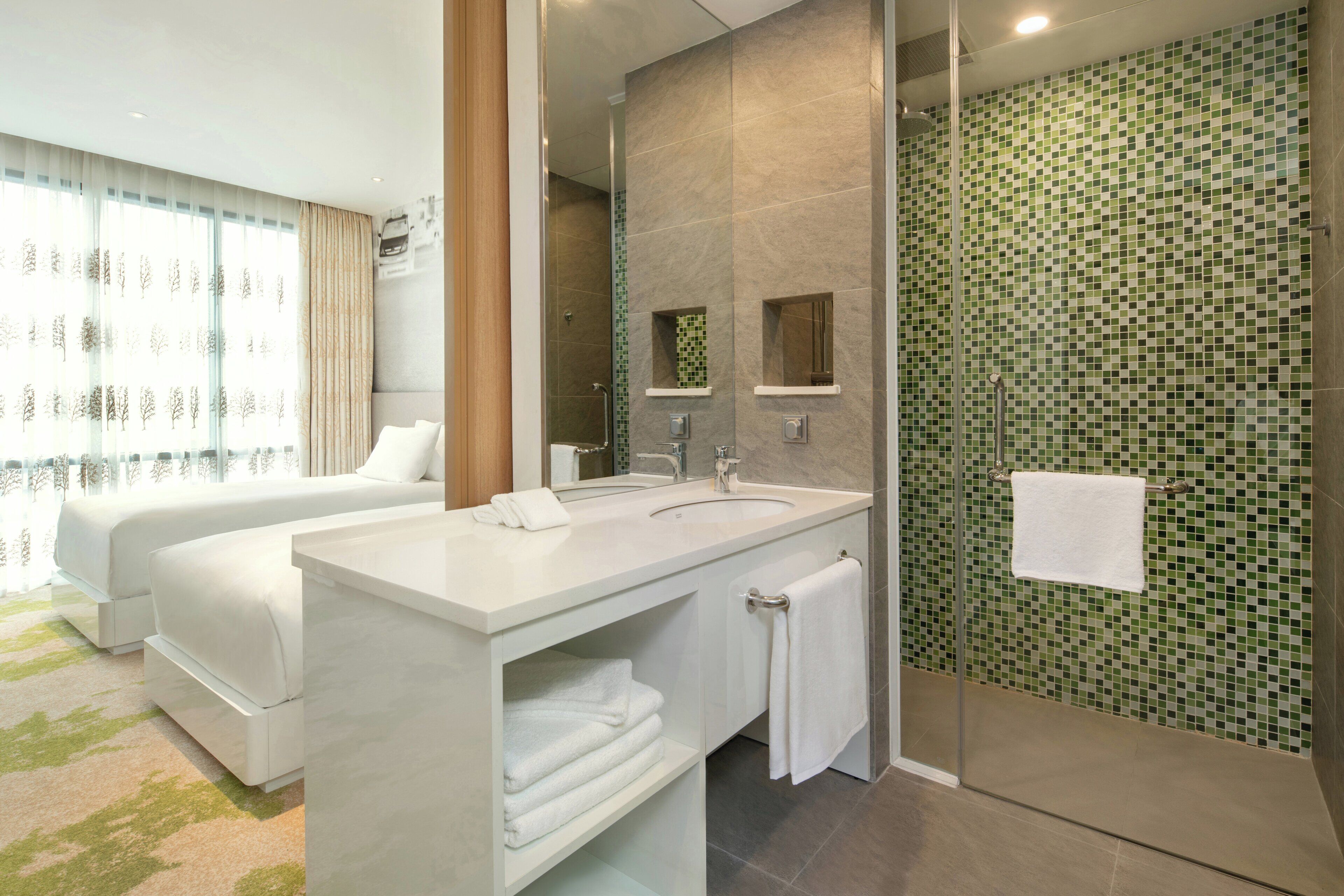 A hotel bathroom with a shower, two sinks, and a large mirror.
