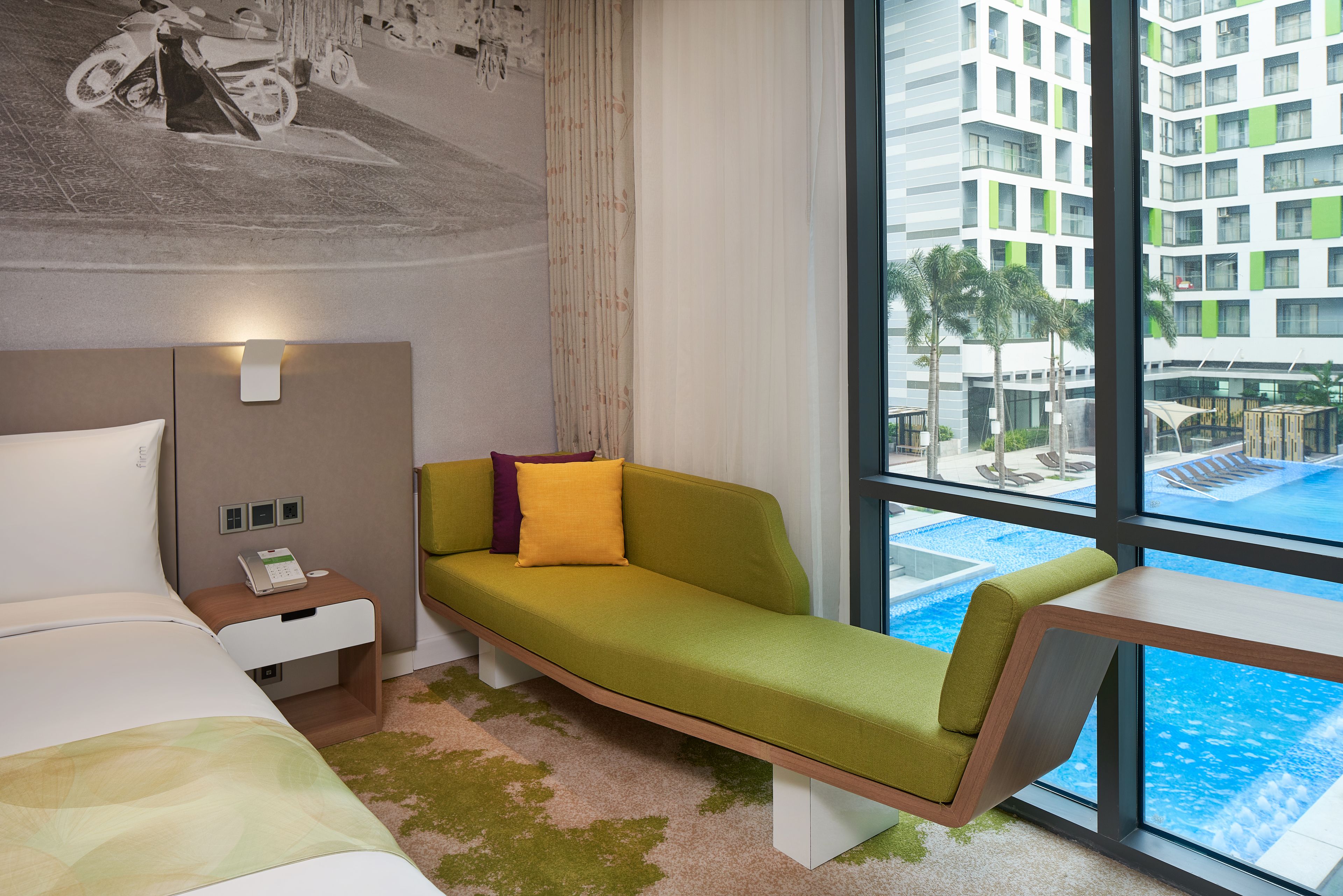 A hotel room with a bed, a green sofa, a small table, a nightstand, a phone, and a view of a swimming pool.