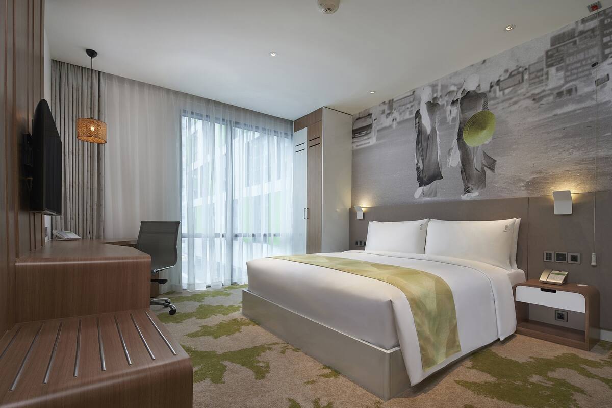 Une chambre d’hôtel moderne équipée d’un grand lit, d’un bureau, d’une chaise, d’une télévision et d’une lampe fixée au mur.