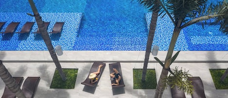 Un área de piscina con sillones reclinables y palmeras.