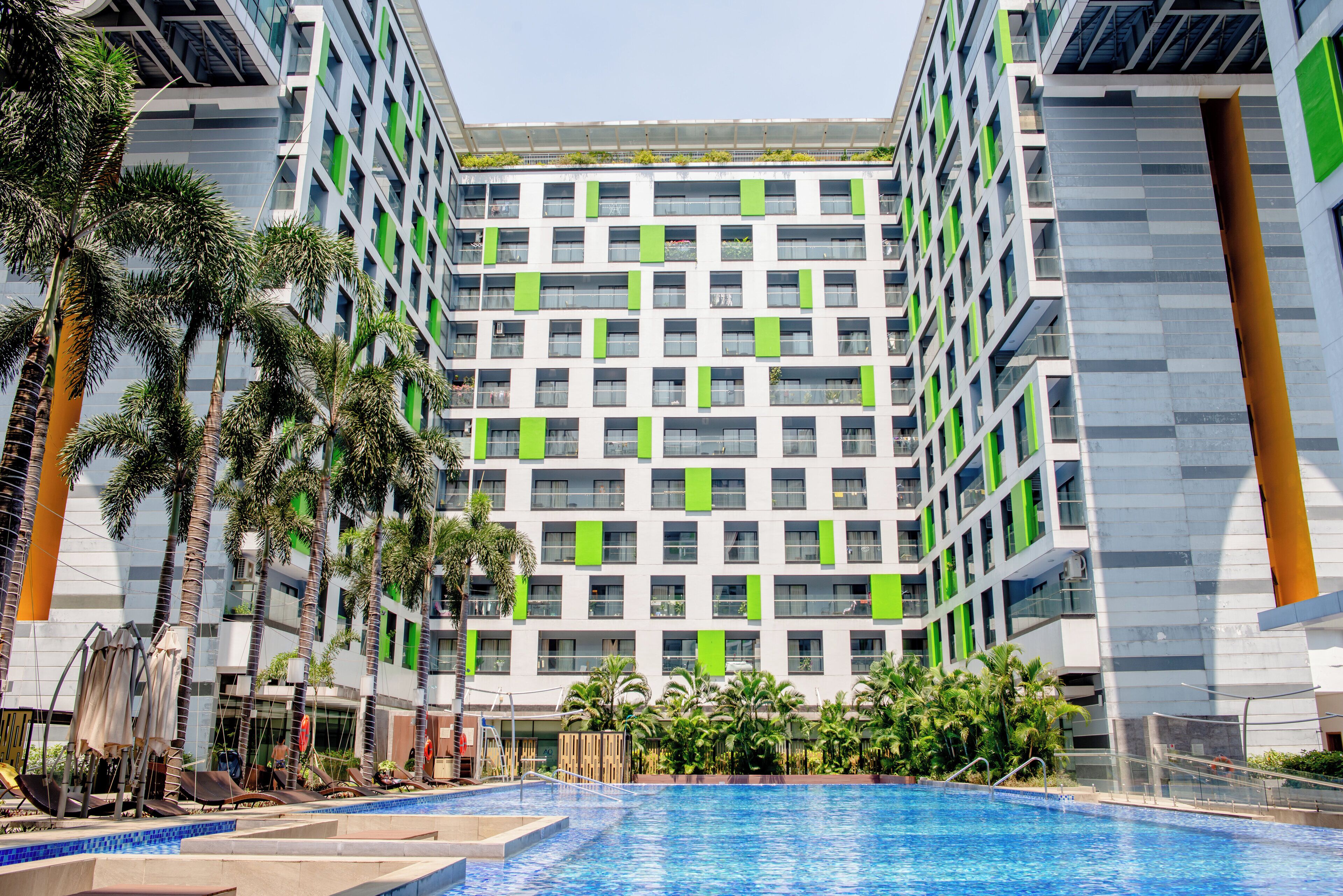 Un hotel modern amb una piscina central, envoltat de palmeres i vegetació.