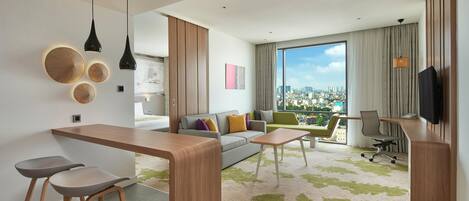 Habitación de hotel moderna con vista a la ciudad, un sofá, una zona de comedor y un televisor.