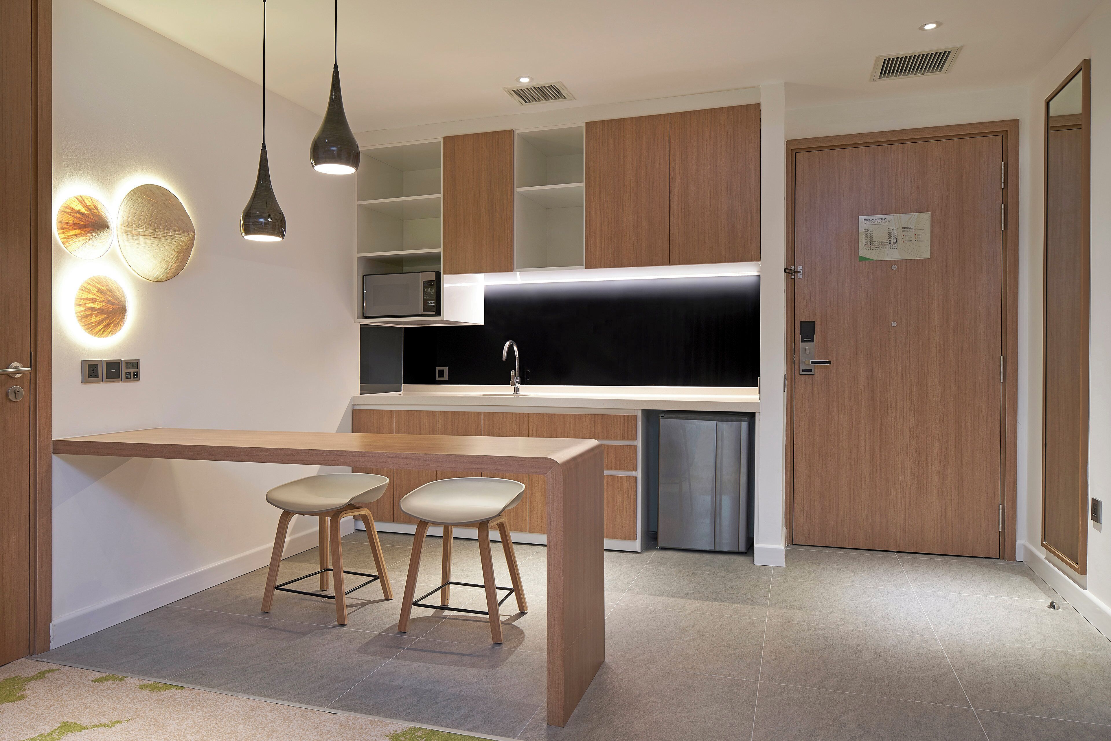 Una cocina moderna con una isla central, taburetes de bar, iluminación colgante y un microondas.