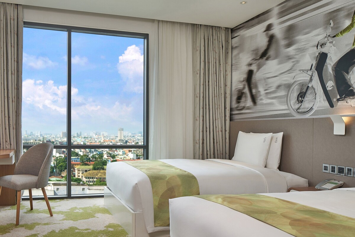 Een hotelkamer met een bed, een stoel, een bureau, een televisie en een groot raam met uitzicht op de stad.