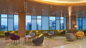 Een moderne lobby met een gebogen houten plafond, grote ramen, groene banken en diverse zithoeken.