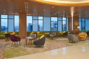 Een moderne lobby met een gebogen houten plafond, grote ramen, groene banken en diverse zithoeken.