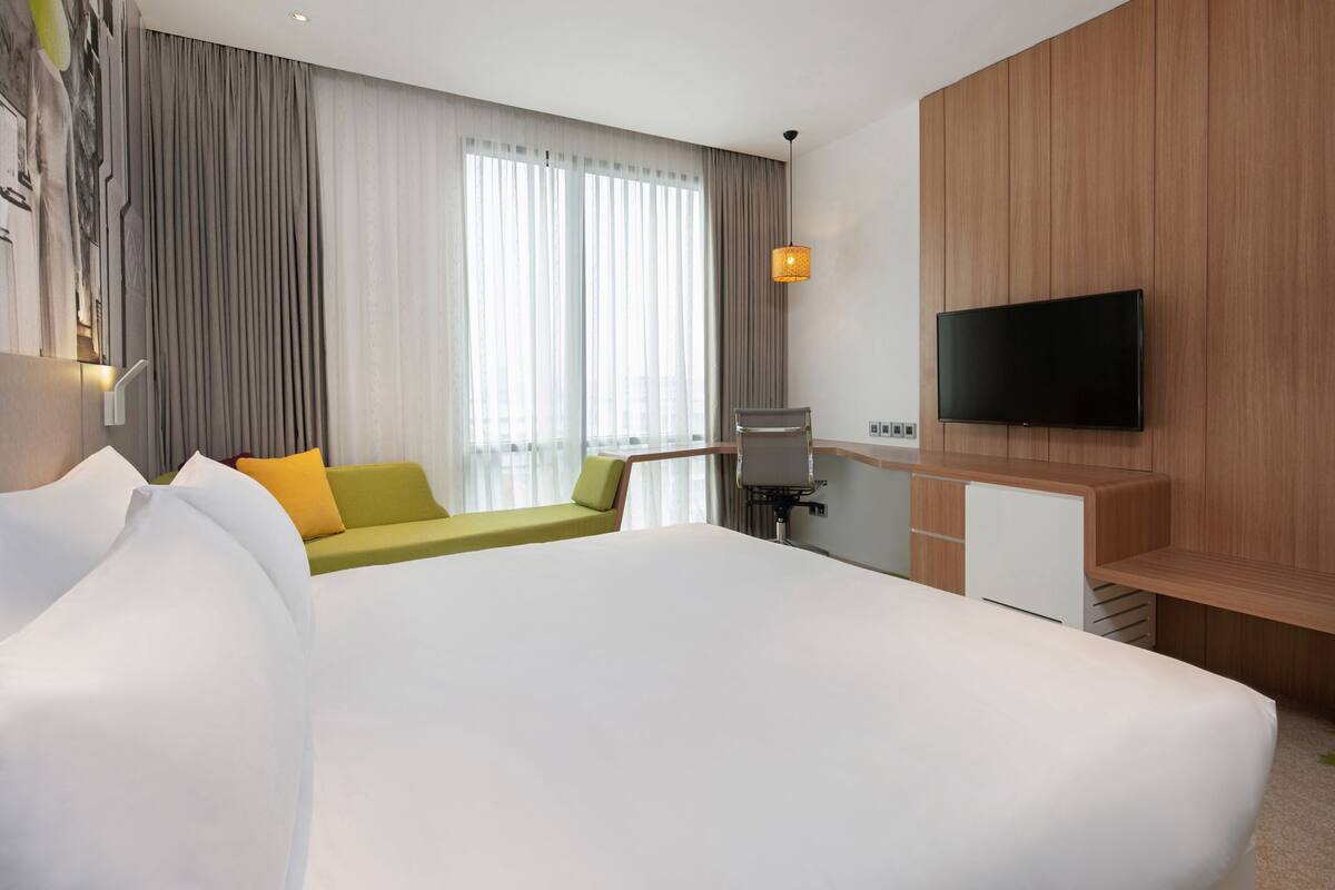 Une chambre d’hôtel avec un grand lit, un bureau doté d’un téléviseur à écran plat, un canapé vert et une grande fenêtre avec des rideaux.