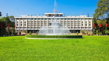A building with a central fountain, surrounded by a well-maintained lawn and palm trees.