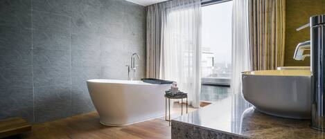 Un baño moderno con una bañera independiente, un lavamanos grande y vistas a la ciudad desde la ventana.
